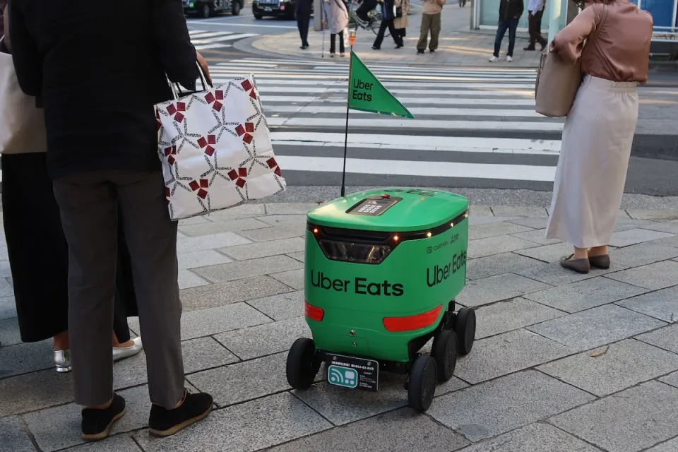 Green Uber Eats delivery robot waits at crosswalk in Tokyo, Japan.